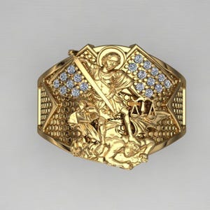 Op de afbeelding: Een gouden ring met een gedetailleerd ontwerp met een figuur van een krijger die een demon bestrijdt. De ring is versierd met heldere zirkonia-stenen.