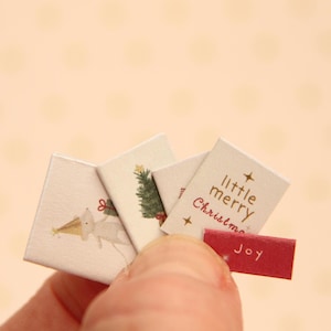 May include: A set of small, rectangular paper cards featuring Christmas illustrations including a mouse in a party hat, a green pine tree, and the text little merry Christmas in gold, accompanied by a small red rectangular tag with the word Joy.