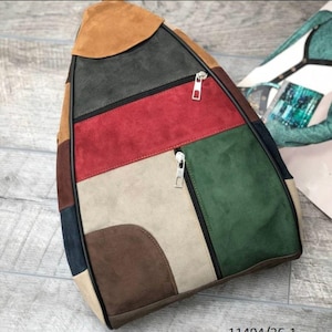 Puede incluir: Mochila de patchwork multicolor con paneles marrones, rojos, verdes y beige. Tiene cierre de cremallera y solapa superior. El material parece ser de ante.