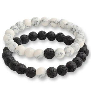 May include: Two bracelets made of black lava rock beads and white marble beads. The bracelets are layered on top of each other.