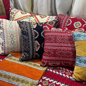 Peut inclure: Un ensemble d'oreillers décoratifs colorés avec des motifs géométriques dans des tons de rouge, orange, jaune, bleu et noir. Les oreillers sont disposés sur un canapé avec un tissu à motifs similaires.