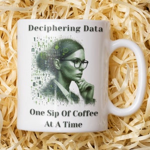 May include: White ceramic mug with the text "Deciphering Data" and "One Sip Of Coffee At A Time". The mug features a green and white illustration of a woman wearing glasses, surrounded by numbers.