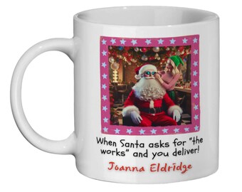Può includere: Tazza in ceramica bianca con un'immagine festosa di Babbo Natale che si fa truccare. L'immagine è incorniciata con un bordo rosa e stelle. Il testo sulla tazza recita: "When Santa asks for "the works" and you deliver! Joanna Eldridge."