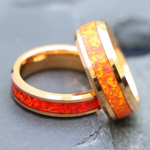 May include: Two gold tungsten carbide rings with a thin band of orange opal inlay. The rings are stacked on top of each other.