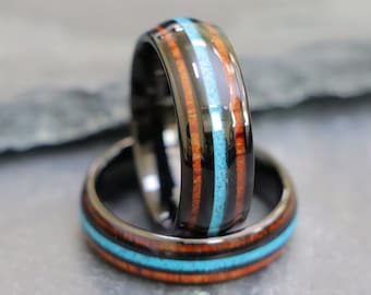 May include: Two black tungsten carbide rings with inlaid wood and turquoise. The rings are stacked on top of each other.