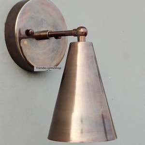 May include: A copper-toned wall sconce with a cone-shaped shade. The sconce has a round base and a simple design.