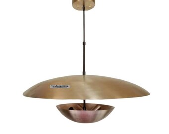 May include: A gold-toned pendant light fixture with a large, flat, circular top and a smaller, bowl-shaped bottom. The light fixture is suspended from a black cord.