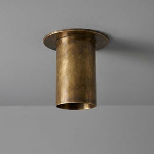 May include: A cylindrical ceiling light fixture with a brushed brass finish. The fixture features a flat circular mounting plate that sits flush against the ceiling, transitioning into a smooth, vertical tube body with an open bottom aperture.