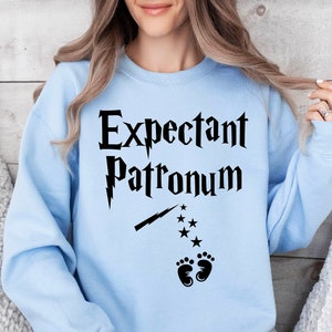 May include: Light blue sweatshirt with the text "Expectant Patronum" in black, a black lightning bolt, and black footprints.