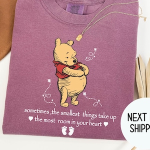 Peut inclure: T-shirt violet avec une illustration de Winnie l'ourson et le texte "sometimes, the smallest things take up ❤ the most room in your heart ❤".