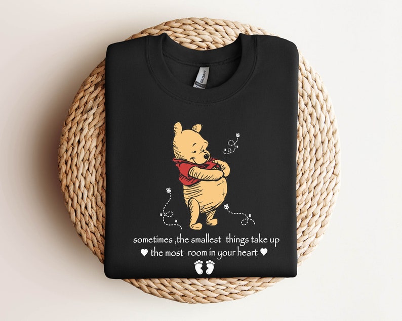 Peut inclure: T-shirt noir avec une illustration de Winnie l'ourson et le texte "sometimes, the smallest things take up the most room in your heart".