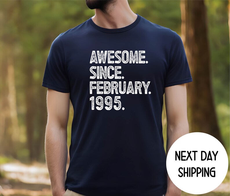 May include: Navy blue t-shirt with the text "AWESOME. SINCE. FEBRUARY. 1995." in white. The shirt has a classic crew neck and short sleeves. The words are stacked vertically. The shirt is worn by a person.