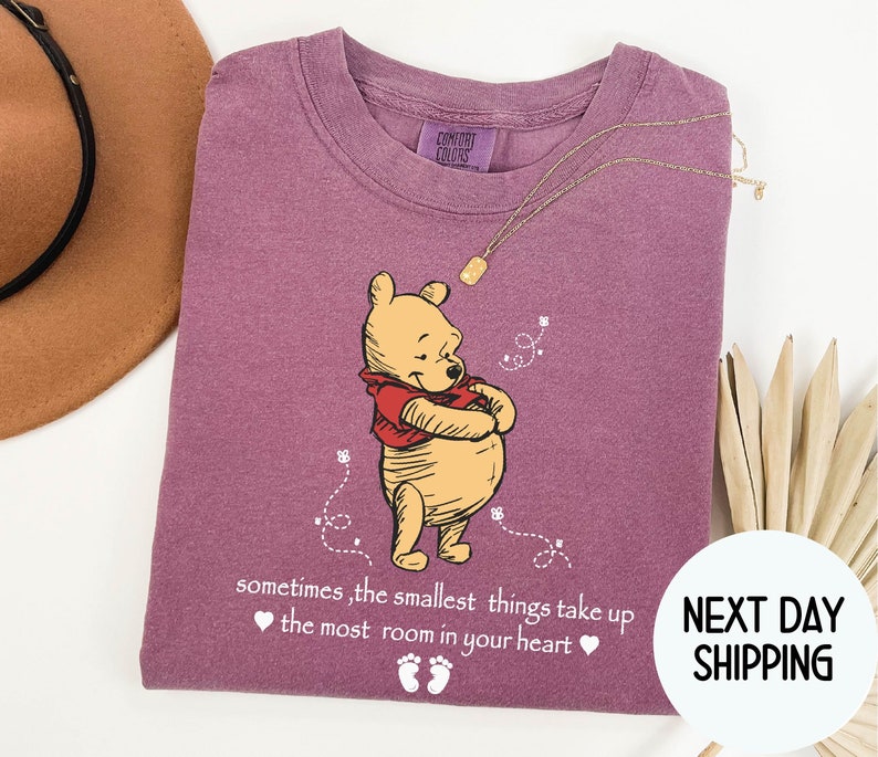 Peut inclure: T-shirt violet avec une illustration de Winnie l'ourson et le texte "sometimes, the smallest things take up ❤ the most room in your heart ❤".