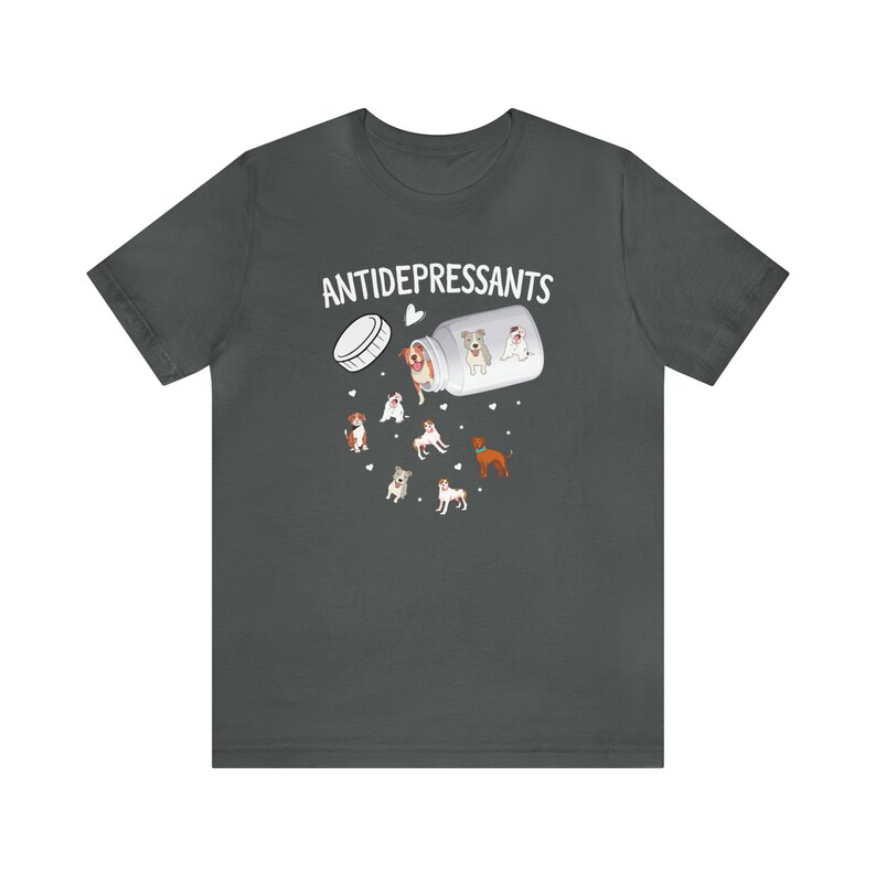May include: Dark gray t-shirt featuring a graphic of a pill bottle labeled "ANTIDEPRESSANTS" with cartoon dogs spilling out. The dogs are various breeds and colors, with hearts scattered around the design. A fun, lighthearted design.
