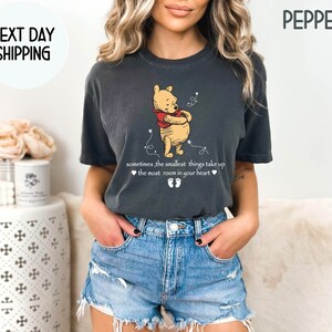 Peut inclure: Un t-shirt gris fonc&eacute; avec une illustration de Winnie l'ourson et le texte "sometimes, the smallest things take up ❤the most room in your heart❤❤" imprim&eacute; sur le devant.