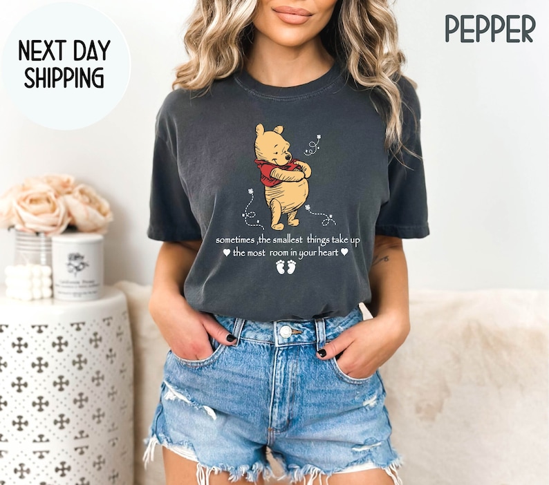Peut inclure: Un t-shirt gris fonc&eacute; avec une illustration de Winnie l'ourson et le texte "sometimes, the smallest things take up ❤the most room in your heart❤❤" imprim&eacute; sur le devant.