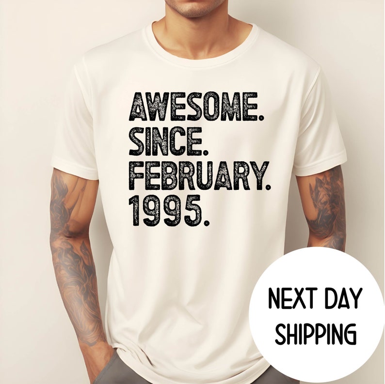 May include: Cream-colored t-shirt with the text "AWESOME. SINCE. FEBRUARY. 1995." in a distressed black font. The shirt is short-sleeved and appears to be made of a soft material. The shirt is being worn by a person.