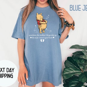 Peut inclure: Un t-shirt en jean bleu avec un motif Winnie l'ourson et le texte "sometimes, the smallest things take up the most room in your heart".