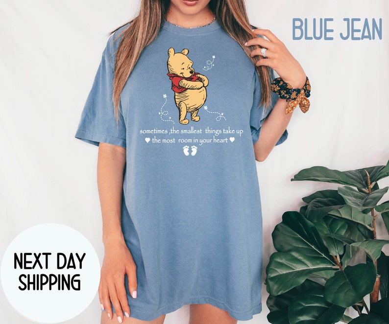 Peut inclure: Un t-shirt en jean bleu avec un motif Winnie l'ourson et le texte "sometimes, the smallest things take up the most room in your heart".