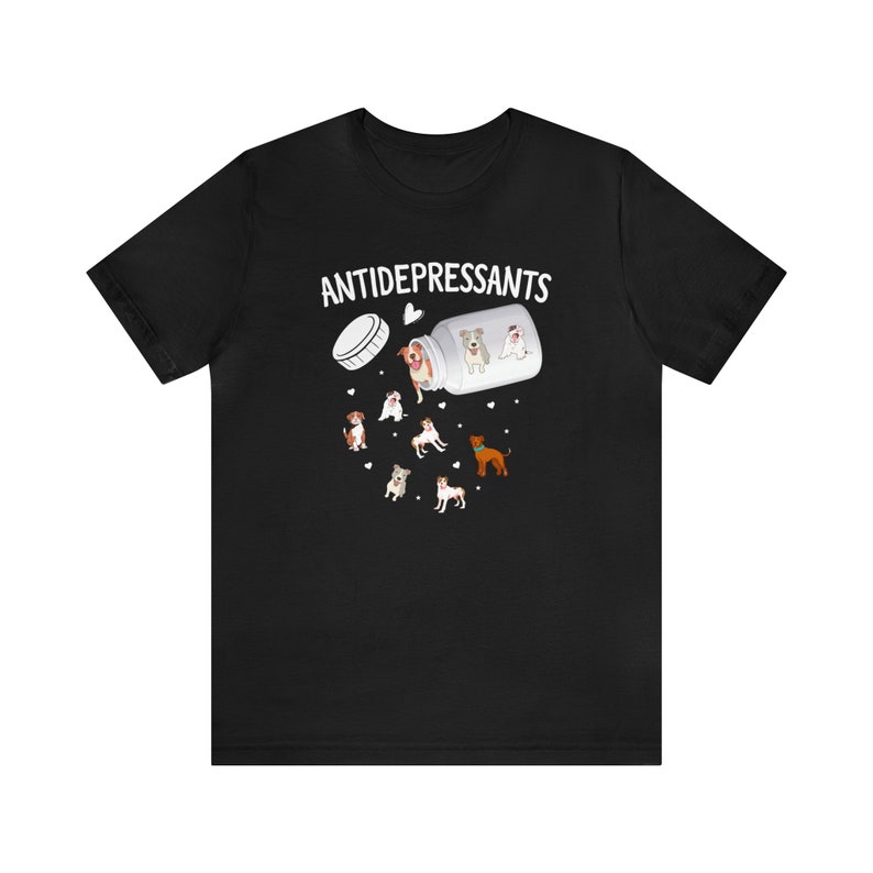 May include: Black t-shirt featuring a graphic of a pill bottle labeled "ANTIDEPRESSANTS" with cartoon dogs spilling out. The design includes various dog breeds and small heart shapes, creating a playful and lighthearted theme.