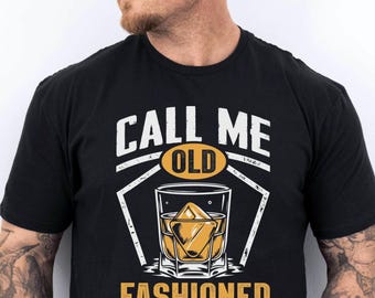 May include: Black t-shirt with a graphic design featuring a whiskey glass with a large ice cube and the words "CALL ME OLD FASHIONED" in white and yellow. The design is centered on the shirt.