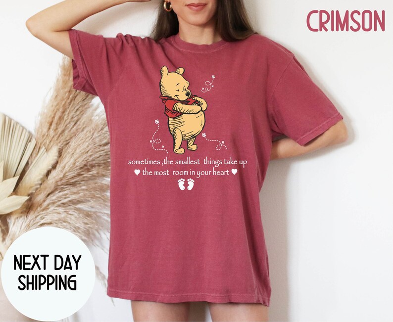 Peut inclure: Un t-shirt rouge fonc&eacute; avec une image de dessin anim&eacute; de Winnie l'ourson et le texte "sometimes, the smallest things take up the most room in your heart".