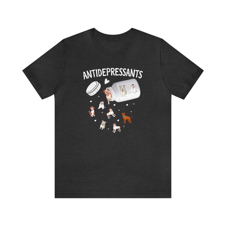 May include: Dark gray t-shirt featuring a graphic of a pill bottle labeled "ANTIDEPRESSANTS" with cartoon dogs spilling out. The design includes various dog breeds and small heart shapes, creating a playful and whimsical aesthetic.