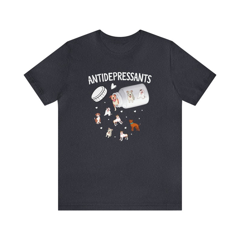 May include: Dark gray t-shirt with the word "ANTIDEPRESSANTS" above a graphic of a pill bottle spilling out cartoon dogs. The dogs are various breeds and colors, with hearts scattered around them.
