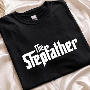 May include: Black t-shirt with the white text "The Stepfather" in a stylized font. The shirt is made of a soft material and is likely a casual wear item.