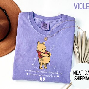 Peut inclure: T-shirt violet avec Winnie l'ourson et la citation "parfois, les plus petites choses prennent le plus de place dans le c&oelig;ur".