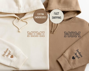 May include: Two hooded sweatshirts, one cream and one brown. The cream sweatshirt has "MIMI" embroidered on the front and "Jackson Angel" on the sleeve. The brown sweatshirt has "MOM" embroidered on the front and "Jackson Angel" on the sleeve.