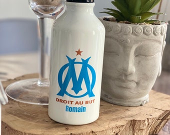 Peut inclure: Une gourde blanche avec un logo bleu et blanc d'une étoile et d'un M. Le texte "DROIT AU BUT Romain" est imprimé sur la gourde.