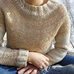 May include: A knitted sweater with a cream and gold color gradient. The sweater has a round neckline and long sleeves.