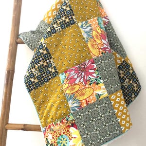 May include: A patchwork quilt featuring a mix of floral and geometric patterns in shades of yellow, green, red, and blue. The quilt is made from cotton fabric and has a soft, fluffy white backing.