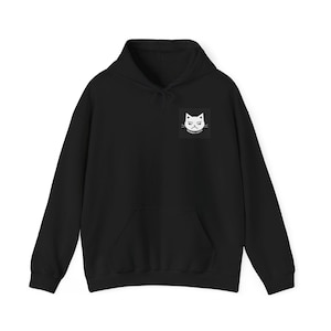 Puede incluir: Una sudadera negra de manga larga con capucha, bolsillo tipo canguro frontal y un pequeño gráfico cuadrado en el pecho izquierdo. El gráfico muestra una ilustración de líneas blancas de un gato con expresión de enfado y el texto GRUMPY KITTY.