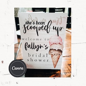 May include: A white card with the text "she's been scooped up" in black cursive lettering. The card also has the text "welcome to fallyn's bridal shower" in black lettering. The card has a watercolor illustration of a three-scoop ice cream cone.