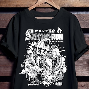 Puede incluir: Camiseta negra con un diseño gráfico blanco que presenta un salmón estilizado con la boca abierta, las palabras "SALMON RUN" y caracteres japoneses. El diseño incluye salpicaduras, engranajes y otros elementos detallados.