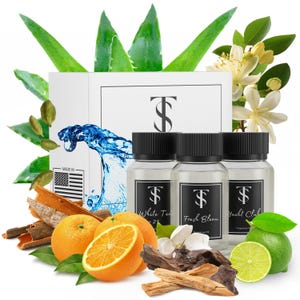 May include: Three glass fragrance oil bottles with black caps, labeled "White Tea", "Fresh Bleau", and "Yacht Club". The bottles are surrounded by oranges, limes, aloe vera, and other botanicals. A box with the letters "TS" is in the background.