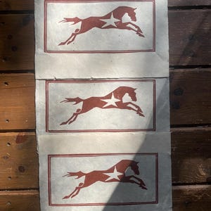 May include: Three rectangular sheets of off-white textured paper, each featuring a dark red block print of a horse in mid-gallop. The horse design includes a white star shape on its flank and is enclosed within a thin dark red rectangular border.