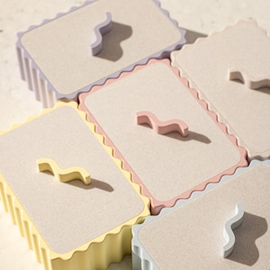 Könnte beinhalten: Fünf dekorative Boxen mit gewellten Kanten und einem wellenförmigen Design in verschiedenen Beige-, Rosa- und Grautönen.