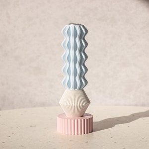 Può includere: Un vaso in ceramica blu e bianco con un design geometrico. Il vaso è impilato su una base rosa con un design geometrico simile.