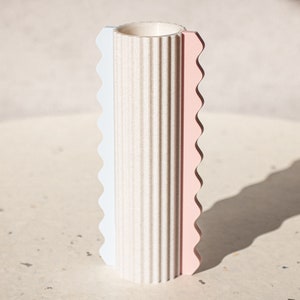 Op de afbeelding: Een witte keramische vaas met een getextureerd oppervlak en een roze en blauw gegolfd ontwerp.