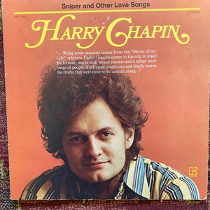 May include: A vintage vinyl record album cover featuring a portrait of Harry Chapin, a singer-songwriter. The album cover is orange with the title "Sniper and Other Love Songs" in white text. The album cover features a quote from the album liner notes.