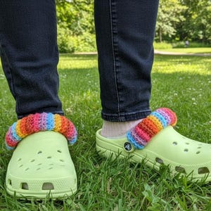 Puede incluir: Zuecos verde claro con bandas de punto a rayas arcoíris. Llevados con vaqueros azul oscuro, los zuecos están sobre una hierba. Las bandas de punto añaden un toque de color a este calzado informal.