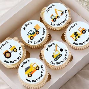 May include: Six cupcakes in a white box, each topped with a circular edible topper featuring construction vehicles and the text Arthur's 5th Birthday Party. The vehicles include an excavator, forklift, cement mixer, tractor, crane, and dump truck.