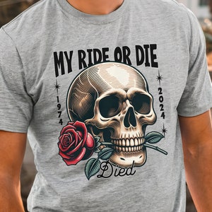 May include: A grey t-shirt with a detailed skull graphic holding a red rose. The text "MY RIDE OR DIE" is above the skull, with "1974" and "2024" on either side. The word "Died" is below the skull.