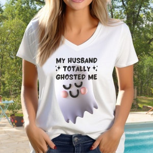 Könnte beinhalten: Weißes V-Ausschnitt-T-Shirt mit dem Text "MY HUSBAND TOTALLY GHOSTED ME" und einem Cartoon-Geist. Der Geist hat ein schwarzes lächelndes Gesicht und rosa Wangen. Das T-Shirt wird von einer Person getragen.