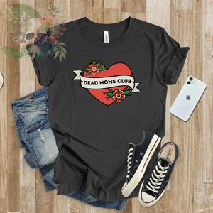 May include: A dark gray t-shirt with a red heart and a banner that reads "Dead Moms Club". The heart has flowers around it.
