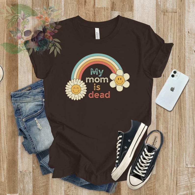 May include: A brown t-shirt with a rainbow and two yellow flowers with smiley faces. The text on the shirt reads "My mom is dead".