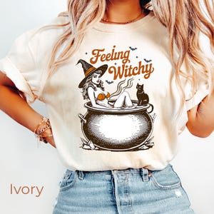 Camiseta de Halloween con un toque de bruja, camiseta retro con caldero de bruja, camiseta con estampado de gato negro de temporada espeluznante, bonita camiseta de otoño con colores acogedores y de brujas.